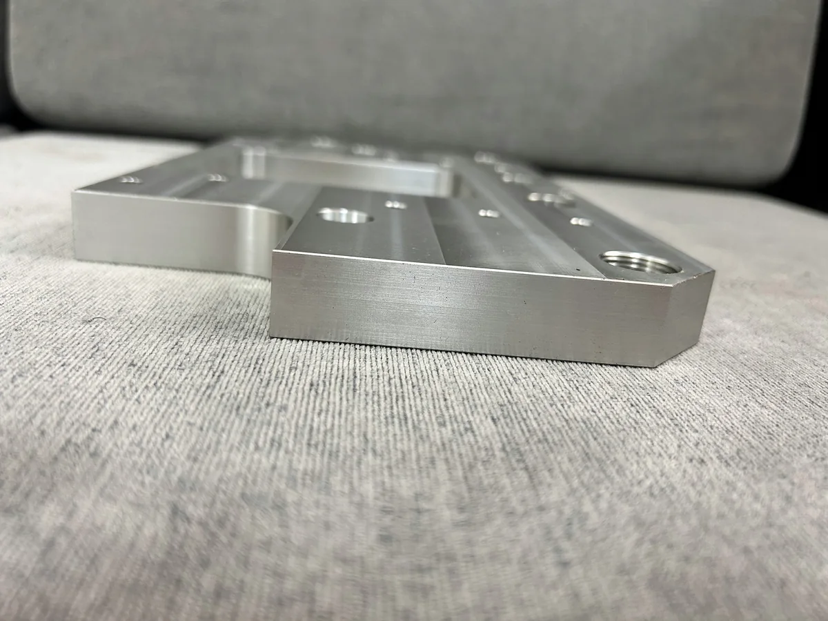 Machined mounting plate with a central rectangular opening and drilled mounting features
